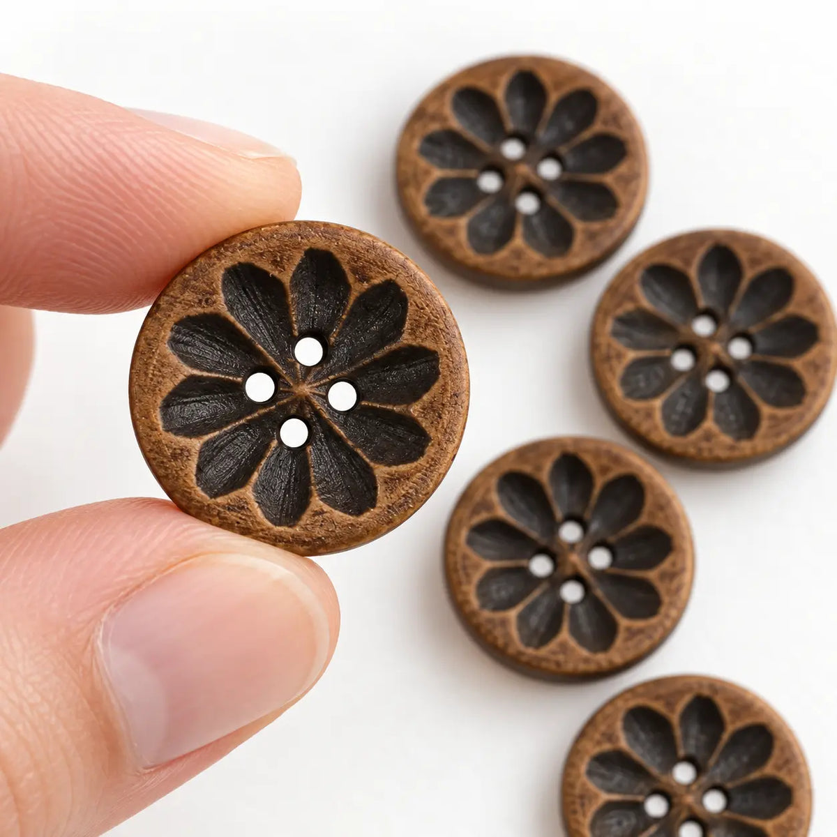 An 18 mm carved wooden four-hole button held between fingertips