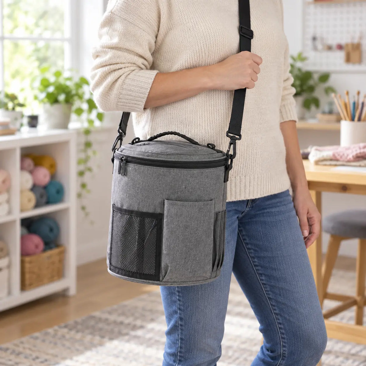Grey cylindrical yarn organizer bag carried at hip height with adjustable shoulder strap