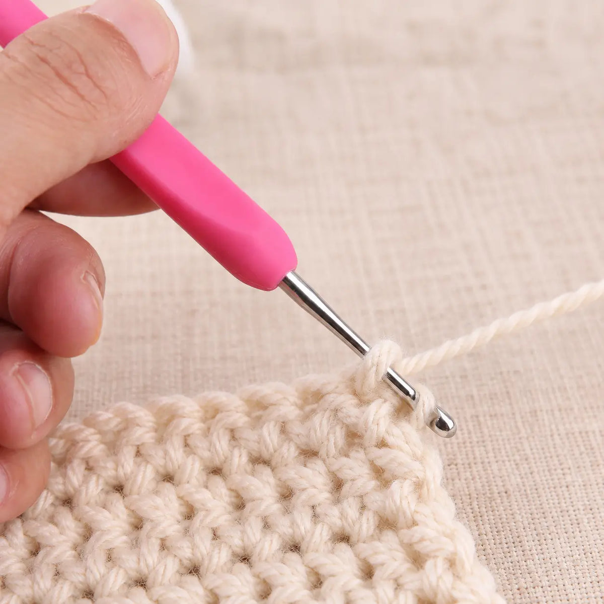 Pink soft-grip crochet hook being used with cream yarn